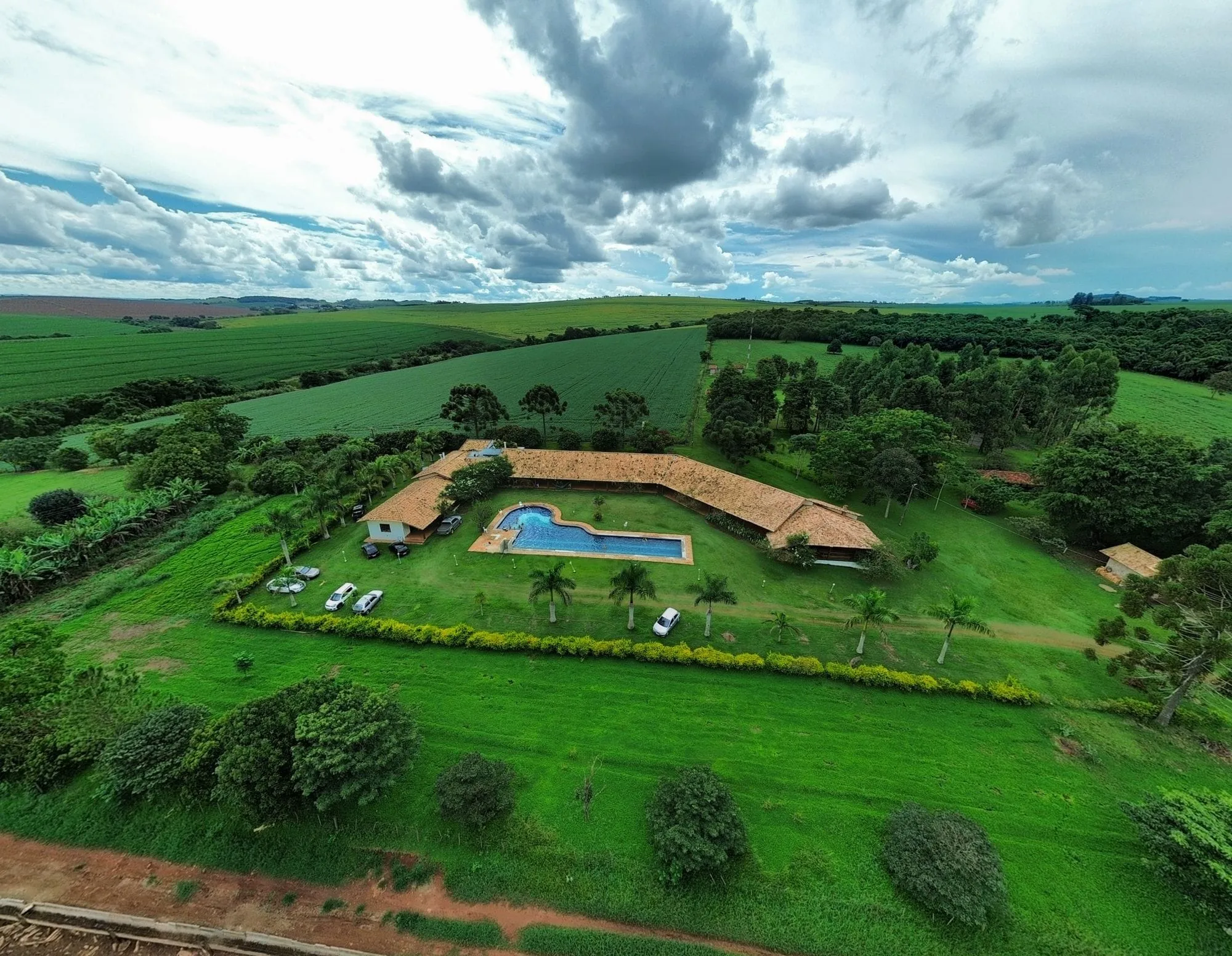 Aerial view of a ranch house and pool surrounded by green fields