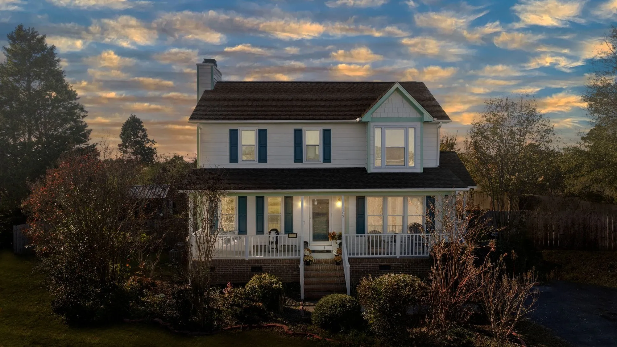 Two-story home with a wraparound porch at sunset