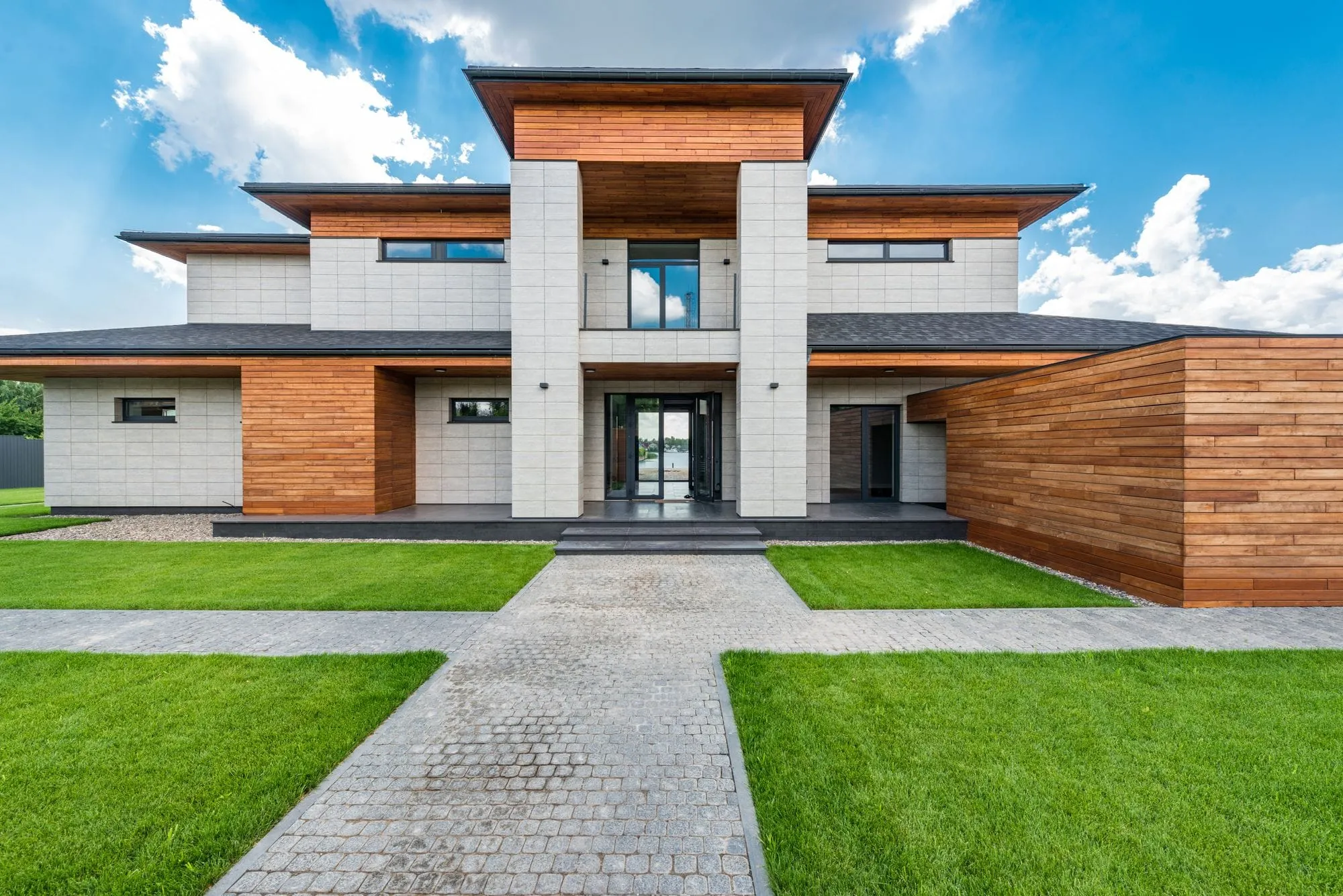 Modern villa with a stone and timber facade behind a long front lawn